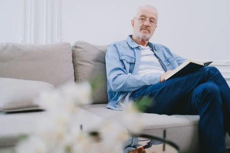 Чоловік у віці 50+ читає книгу в окулярах у світлій вітальні